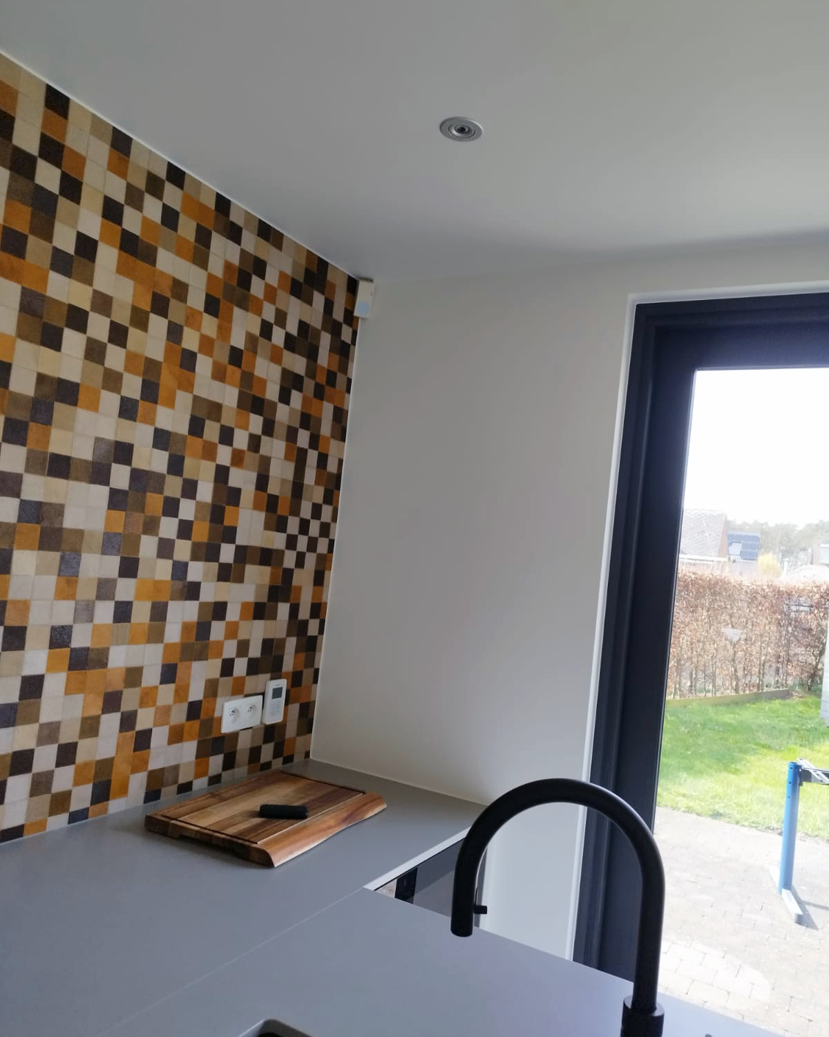 Keuken met decoratief mozaïekbehang en professioneel afgewerkte muren en plafond.