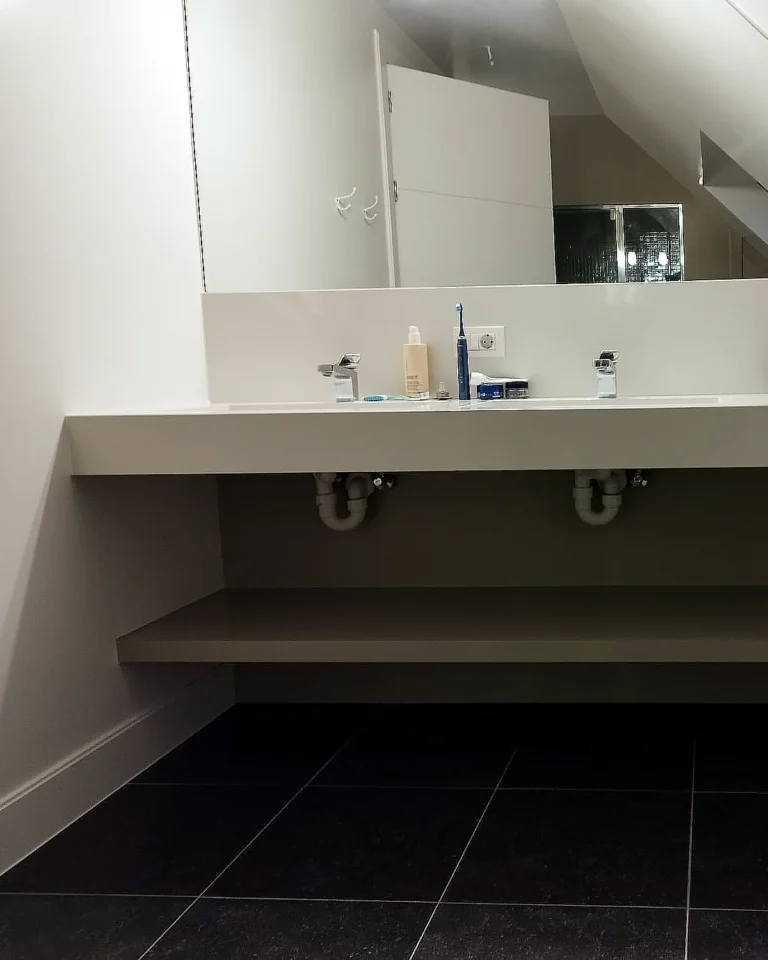 Professioneel binnenschilderwerk in een badkamer op zolder met strak afgewerkte muren, spiegel en wastafel.