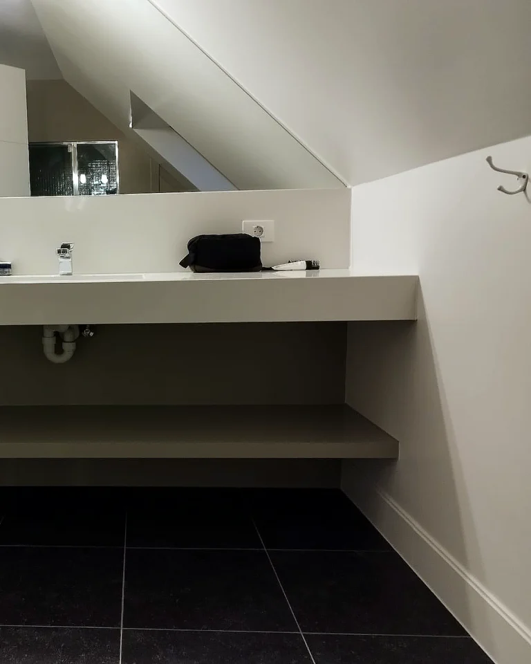 Badkamer op zolder met gelakte houten plank onder de wastafel, strak afgewerkte muren en professioneel binnenschilderwerk.