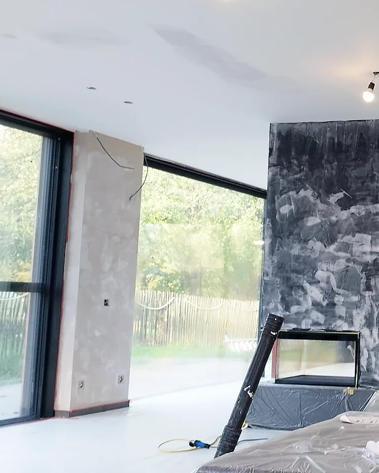 Professionele voorbereiding van muren en plafond in de woonkamer met pleisterwerk en schuurwerk vóór binnenschilderwerken.
