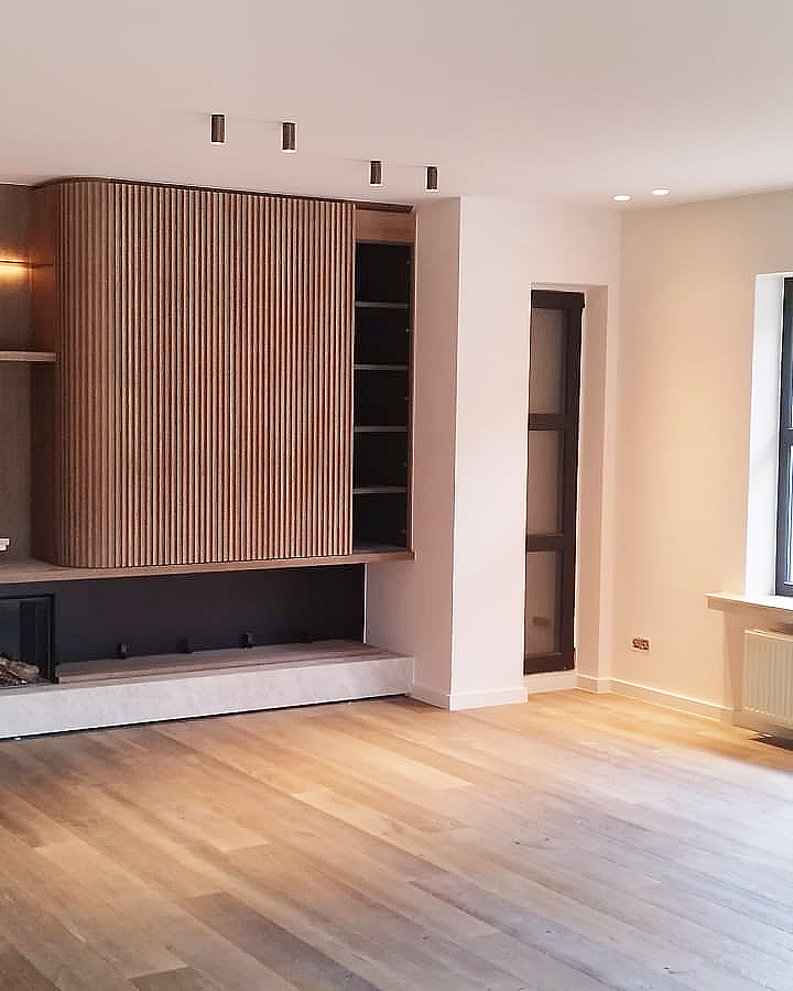 Afgewerkte leefruimte met strak schilderwerk, houten maatwerk en lichte muren.