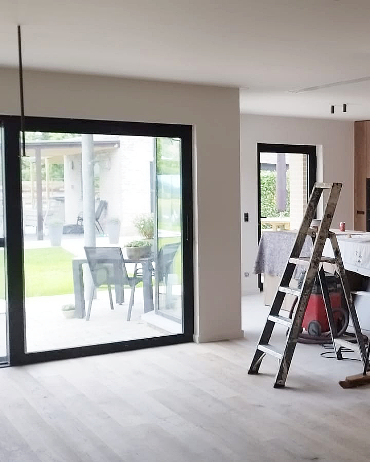 Strak geschilderde binnenwand naast een grote zwarte raampartij in een modern interieur.