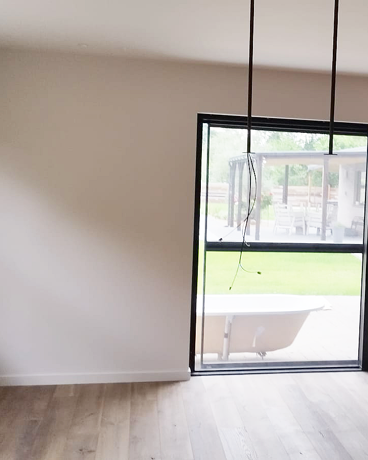 Strak geschilderde binnenwand naast een grote zwarte raampartij in een modern interieur.