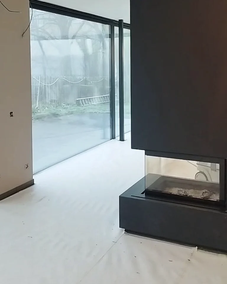 Glad afgewerkte en geschilderde wand rond moderne haard na plamuurwerken, met zorgvuldig beschermde vloer tijdens de schilderwerken.