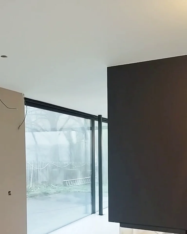 Strak gestucte en geschilderde wand boven moderne haard na professionele plamuur- en schilderwerken.